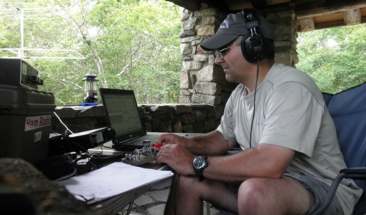 A man has a radio set up outside and is wearing headphones.